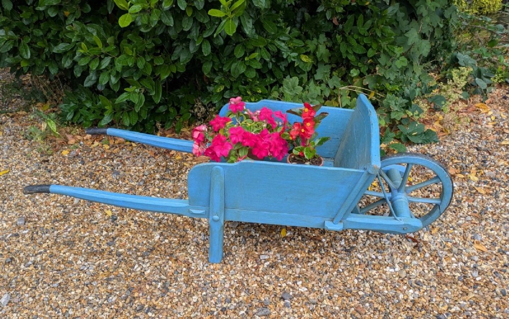 A 19th-century hand-crafted light blue painted wooden garden wheelbarrow with a spoked wheel resting on a gravel surface. View II