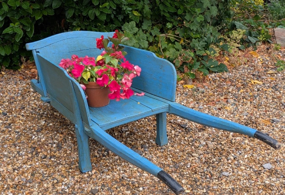 A 19th-century hand-crafted light blue painted wooden garden wheelbarrow with a spoked wheel resting on a gravel surface. View V