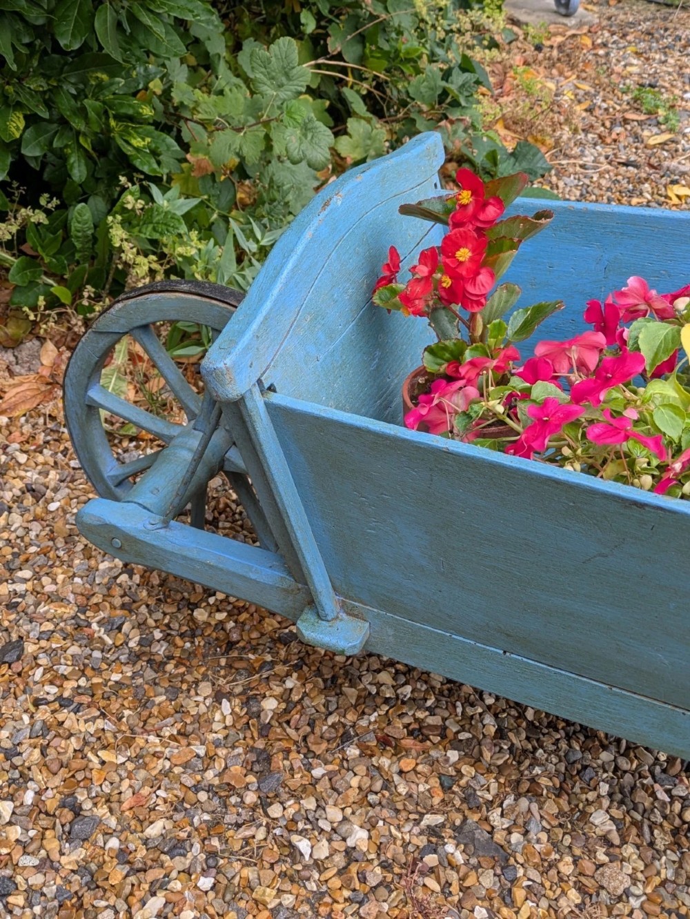 A 19th-century hand-crafted light blue painted wooden garden wheelbarrow with a spoked wheel resting on a gravel surface. View VI