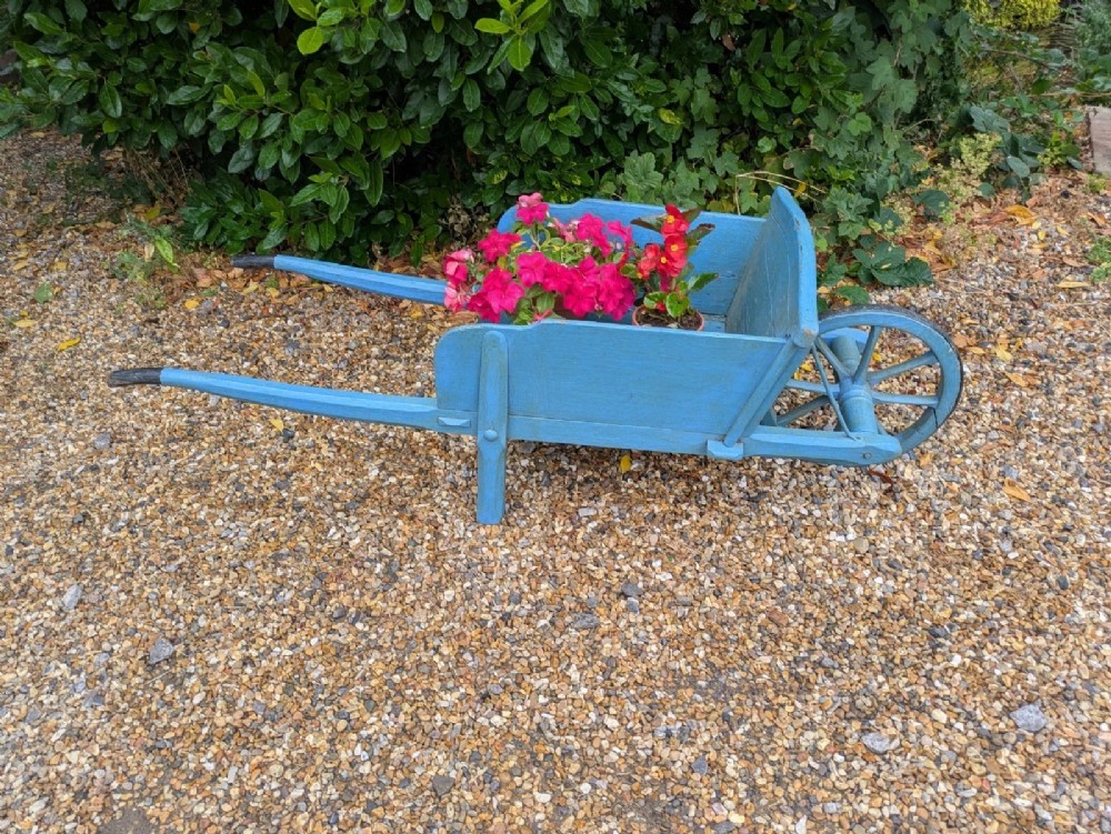 A 19th-century hand-crafted light blue painted wooden garden wheelbarrow with a spoked wheel resting on a gravel surface. View VIII