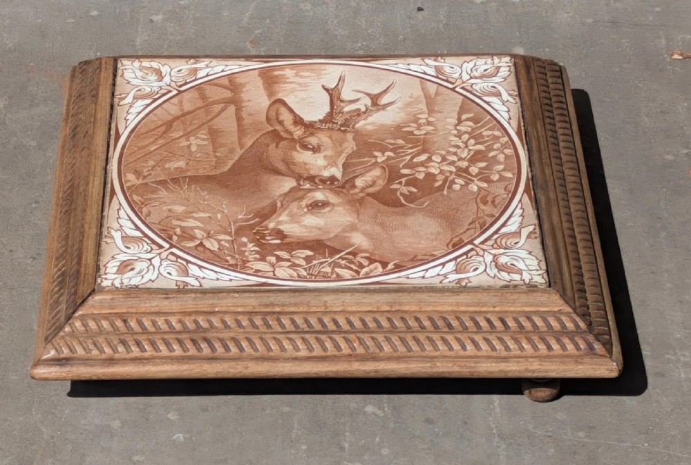A square antique ceramic tile depicting a stag and doe in a woodland setting, framed within carved oak rope-twist moulding. View III