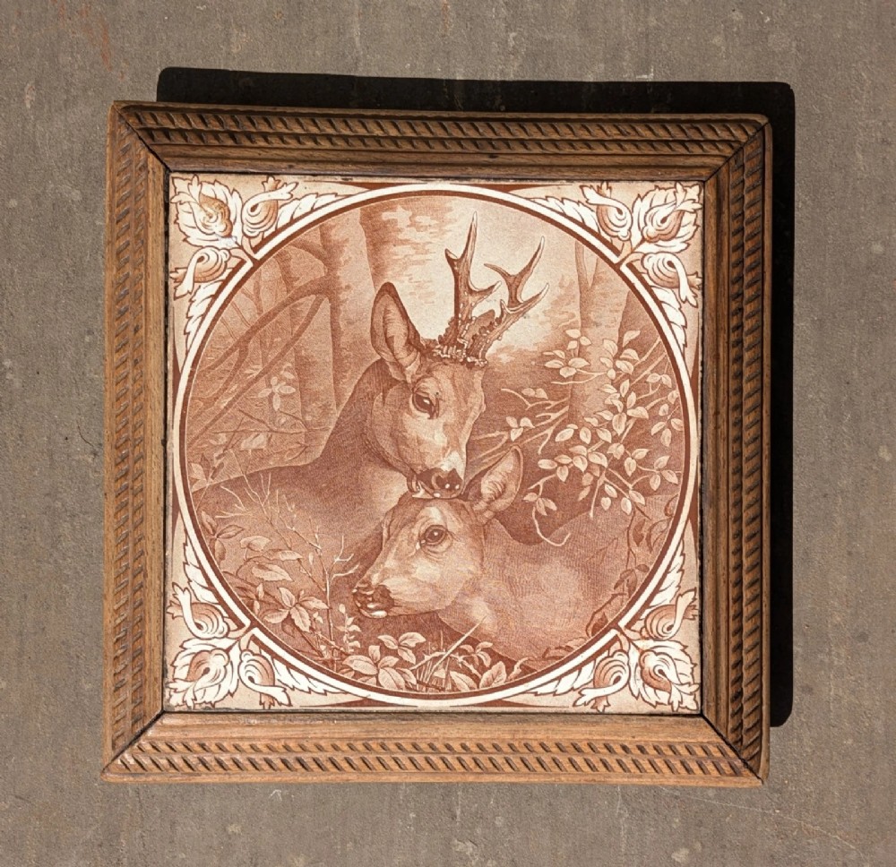 A square antique ceramic tile depicting a stag and doe in a woodland setting, framed within carved oak rope-twist moulding. View VII