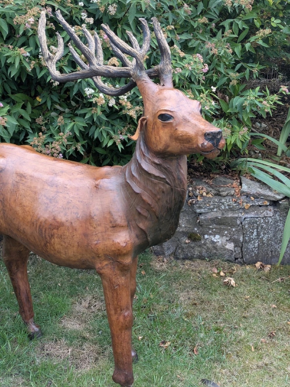 A life-like standing buck deer sculpture wrapped in warm brown stitched leather featuring large branching antlers and inset dark eyes. View II