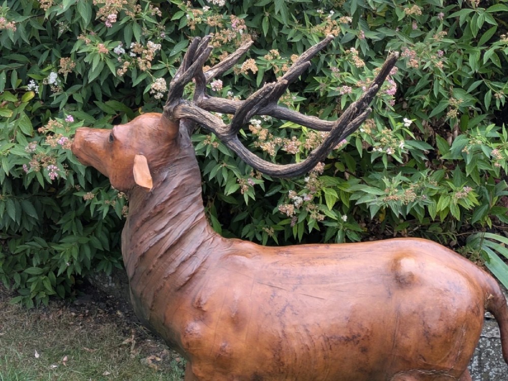 A life-like standing buck deer sculpture wrapped in warm brown stitched leather featuring large branching antlers and inset dark eyes. View III