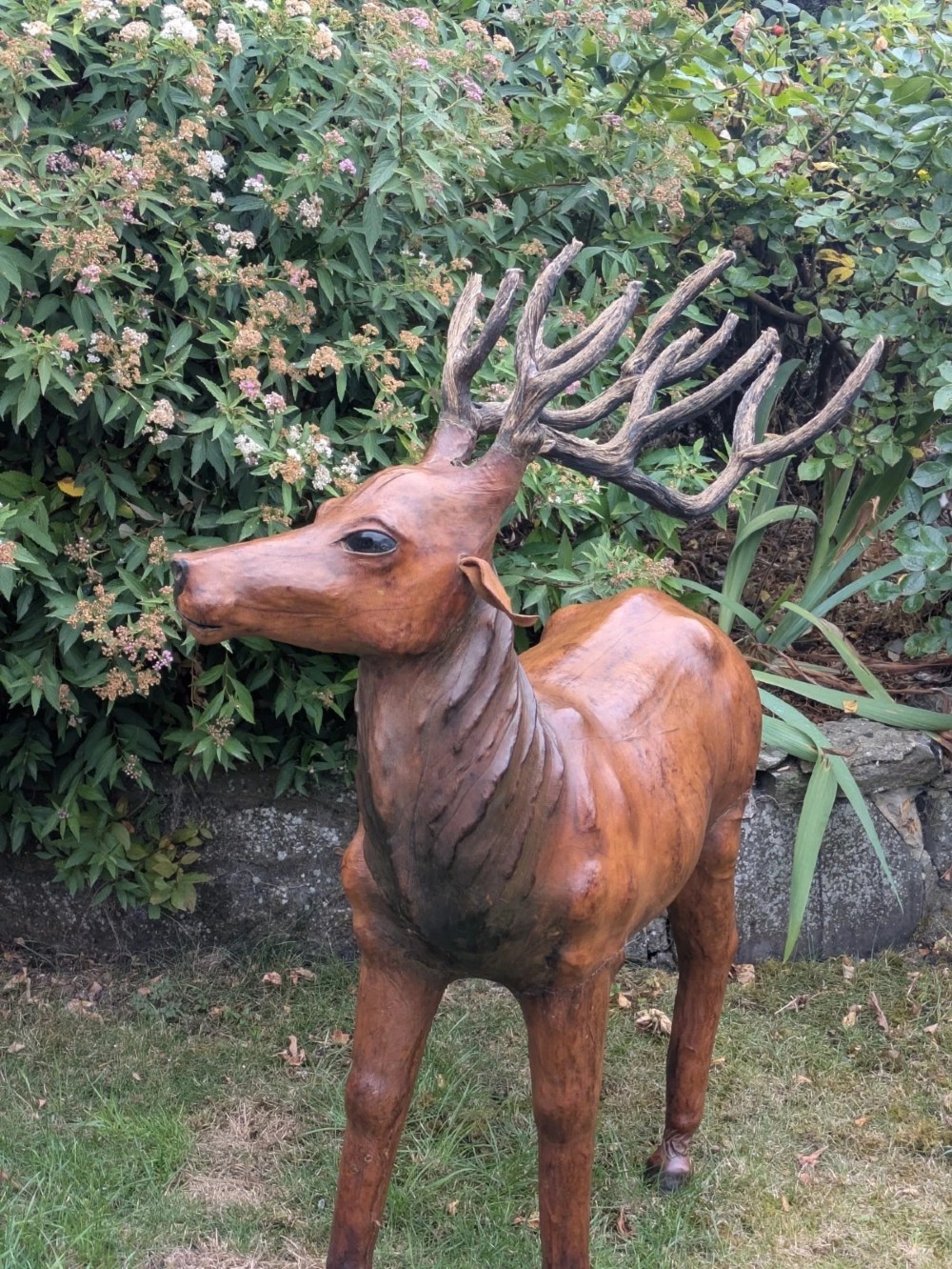 A life-like standing buck deer sculpture wrapped in warm brown stitched leather featuring large branching antlers and inset dark eyes. View X
