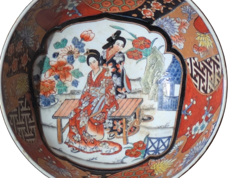 A deep round Japanese Imari porcelain bowl decorated with iron red, blue, green, and gold painted patterns featuring central figural cartouches and floral motifs. View X