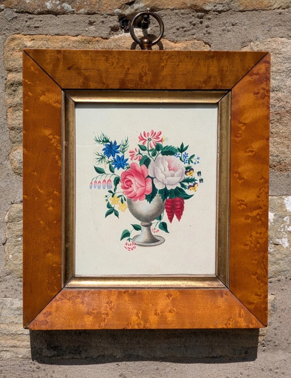 A framed Regency watercolour painting depicting a vibrant floral bouquet in an urn, set within a wide burr wood frame featuring a brass suspension ring.