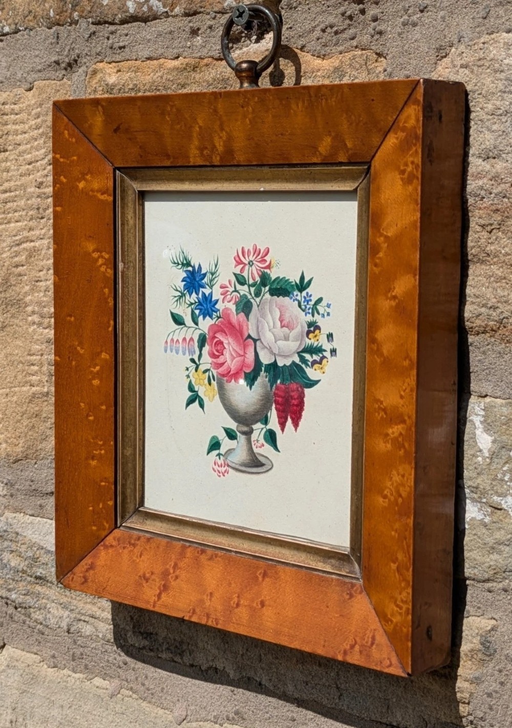 A framed Regency watercolour painting depicting a vibrant floral bouquet in an urn, set within a wide burr wood frame featuring a brass suspension ring. View IV