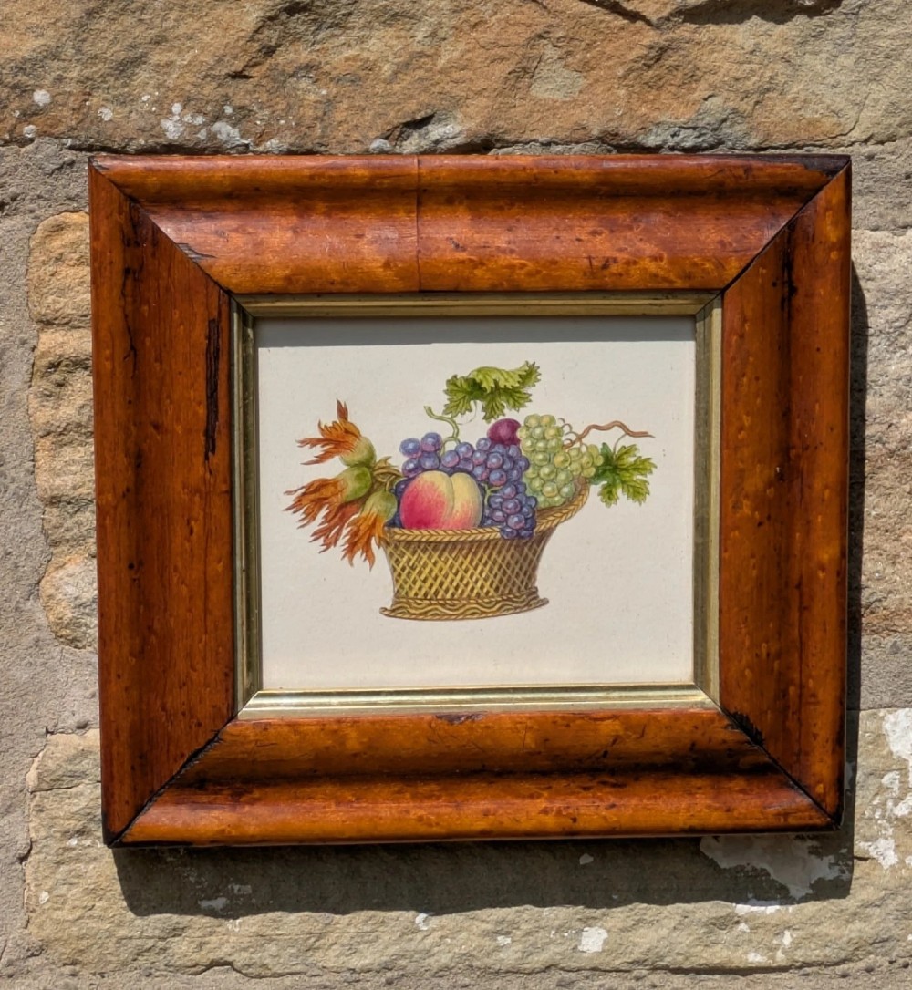 A nineteenth-century watercolour illustration depicting a woven basket filled with grapes, peaches, and hazelnuts, presented in a wide maple veneer frame with a gilded inner slip.