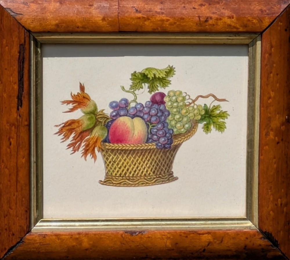 A nineteenth-century watercolour illustration depicting a woven basket filled with grapes, peaches, and hazelnuts, presented in a wide maple veneer frame with a gilded inner slip. View IV
