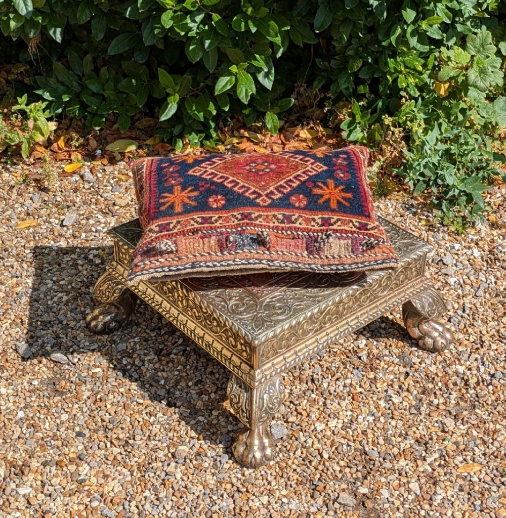 A square antique Indian low table with embossed brass and copper metal cladding, floral foliage motifs, a central geometric panel, and four claw feet. View II