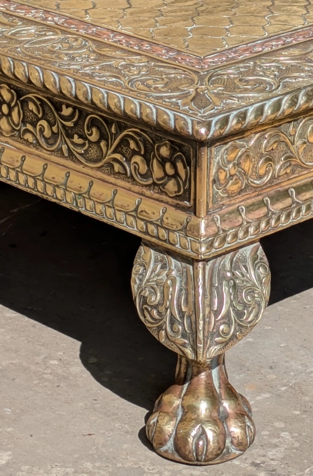 A square antique Indian low table with embossed brass and copper metal cladding, floral foliage motifs, a central geometric panel, and four claw feet. View VII