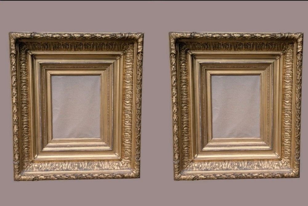 A matching pair of deep profile Victorian gilt picture frames featuring layered cove moulding and carved leaf border details.
