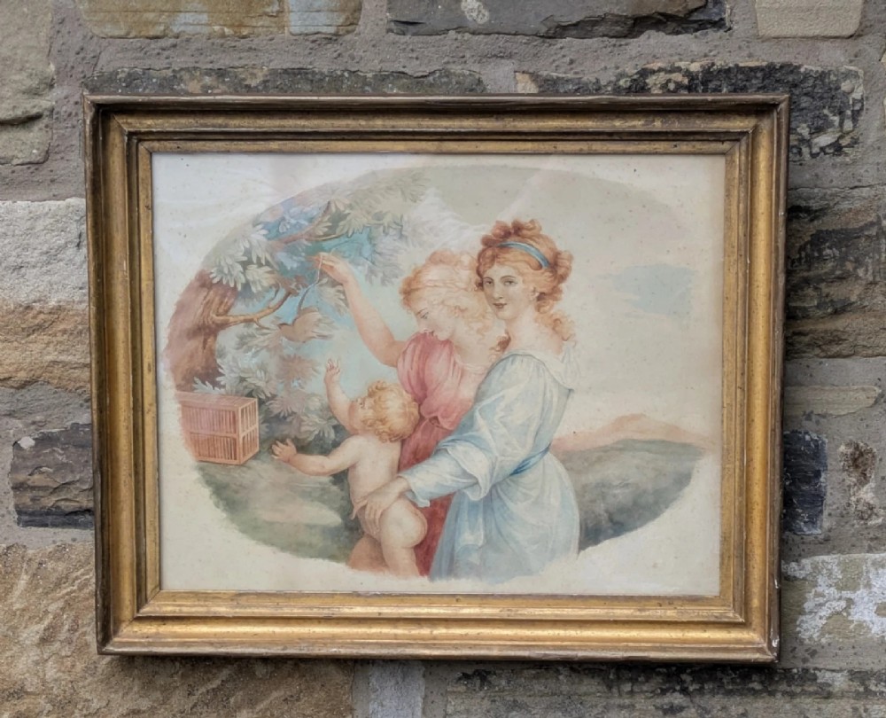 A framed classical watercolour painting depicting two draped female figures and a child beneath trees, presented in a moulded gilt frame.