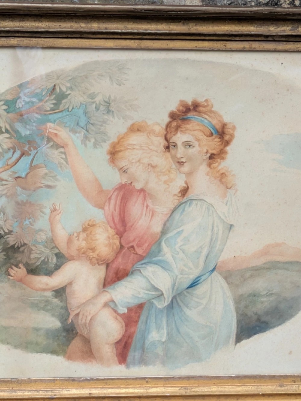 A framed classical watercolour painting depicting two draped female figures and a child beneath trees, presented in a moulded gilt frame. View VII