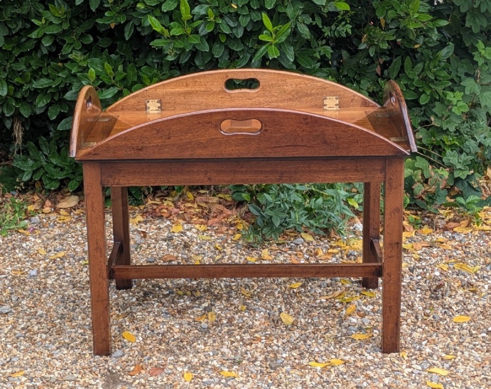 An oval mahogany butlers tray coffee table featuring drop-down hinged sides with hand-cut handles and brass hinges, resting on a four-legged base with side stretchers. View II