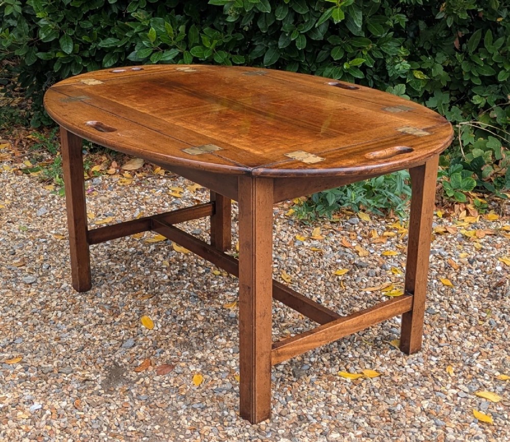 An oval mahogany butlers tray coffee table featuring drop-down hinged sides with hand-cut handles and brass hinges, resting on a four-legged base with side stretchers. View V