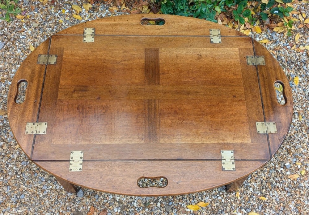 An oval mahogany butlers tray coffee table featuring drop-down hinged sides with hand-cut handles and brass hinges, resting on a four-legged base with side stretchers. View VI