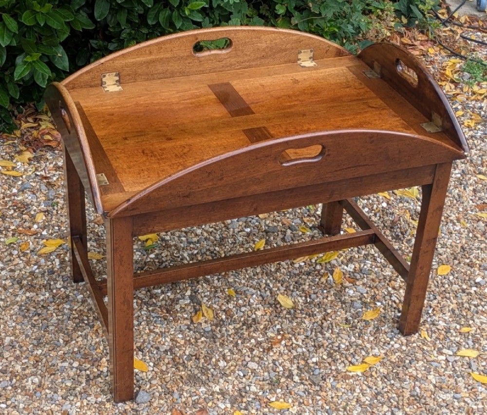 An oval mahogany butlers tray coffee table featuring drop-down hinged sides with hand-cut handles and brass hinges, resting on a four-legged base with side stretchers. View VII