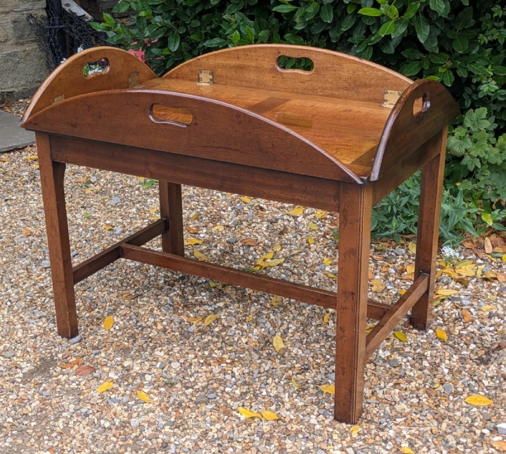 An oval mahogany butlers tray coffee table featuring drop-down hinged sides with hand-cut handles and brass hinges, resting on a four-legged base with side stretchers. View IX