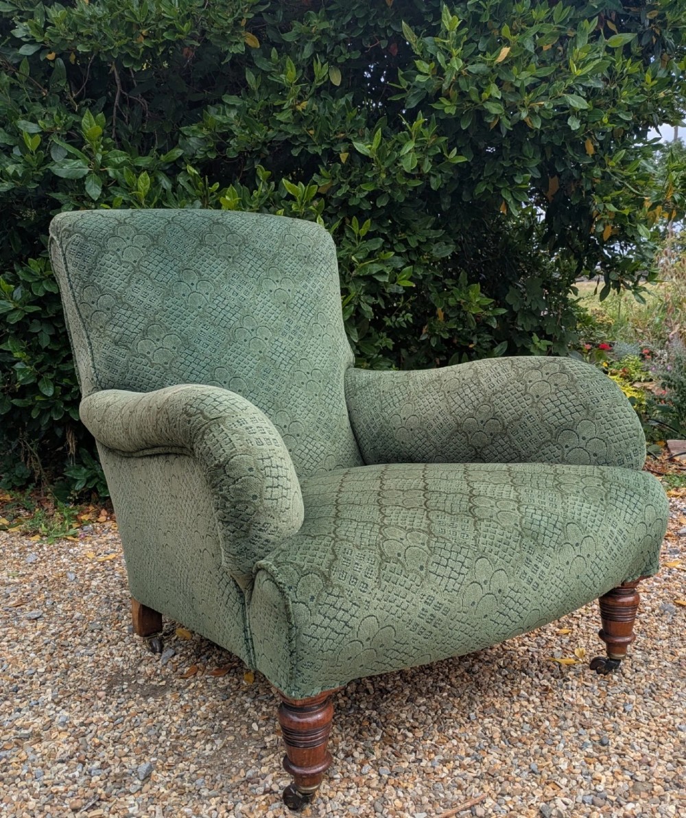 A low-slung 19th-century Howard style armchair upholstered in patterned green fabric with turned mahogany front legs and brass castors.
