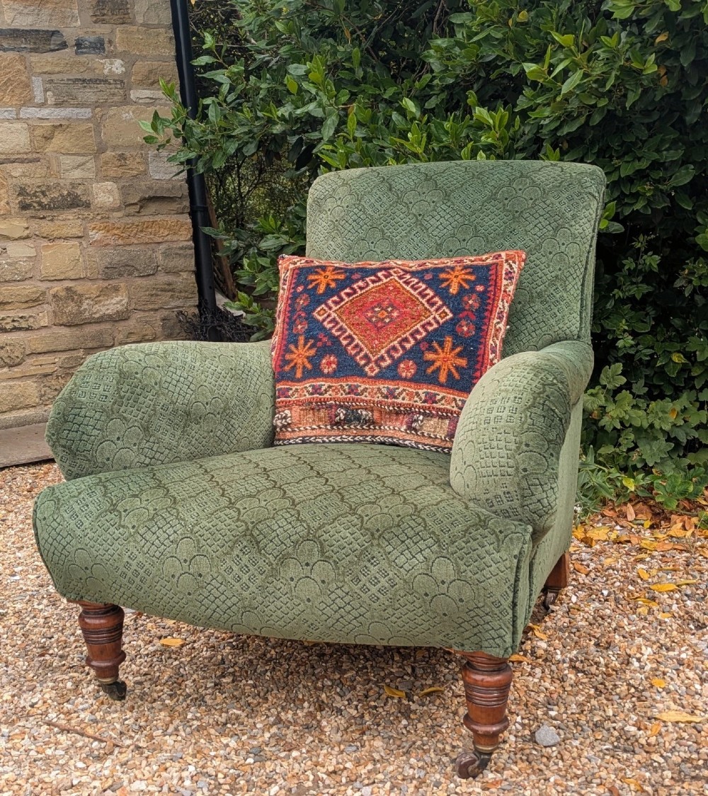 A low-slung 19th-century Howard style armchair upholstered in patterned green fabric with turned mahogany front legs and brass castors. View II
