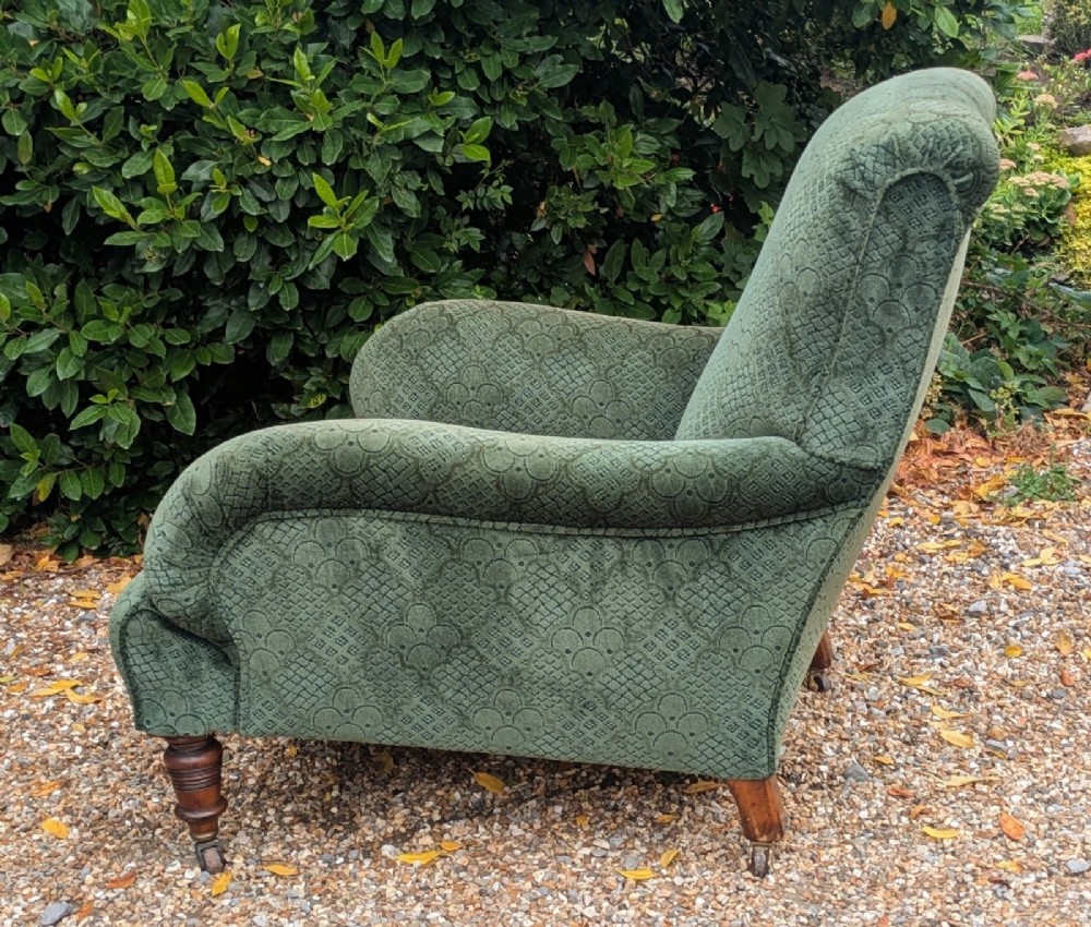A low-slung 19th-century Howard style armchair upholstered in patterned green fabric with turned mahogany front legs and brass castors. View III