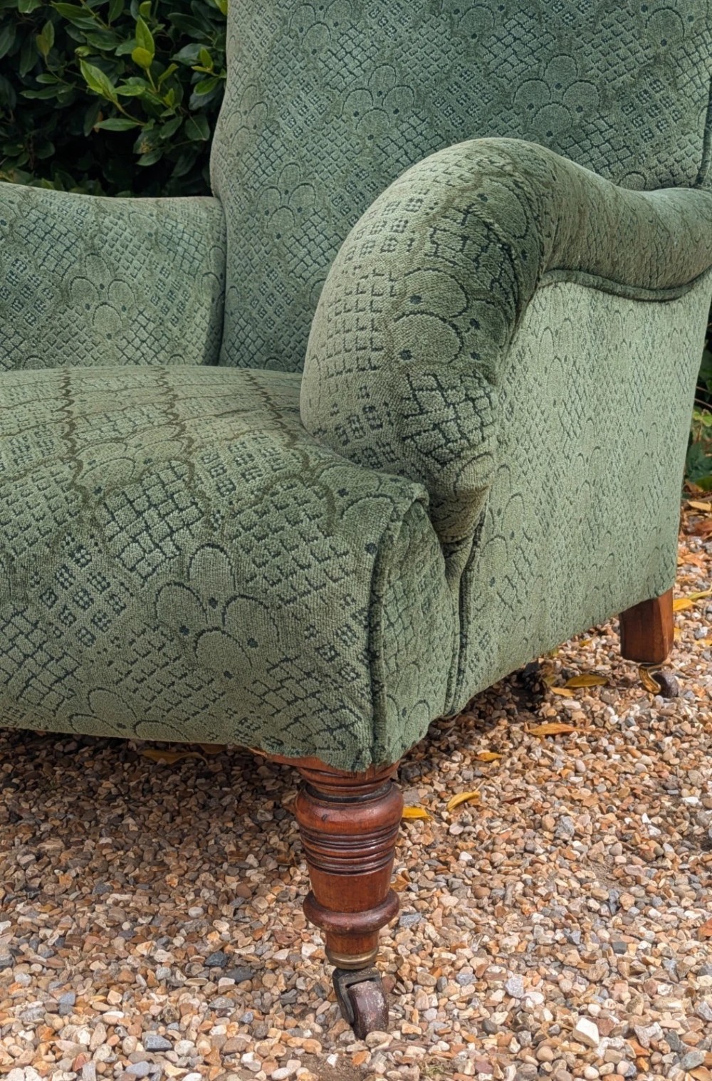 A low-slung 19th-century Howard style armchair upholstered in patterned green fabric with turned mahogany front legs and brass castors. View IV