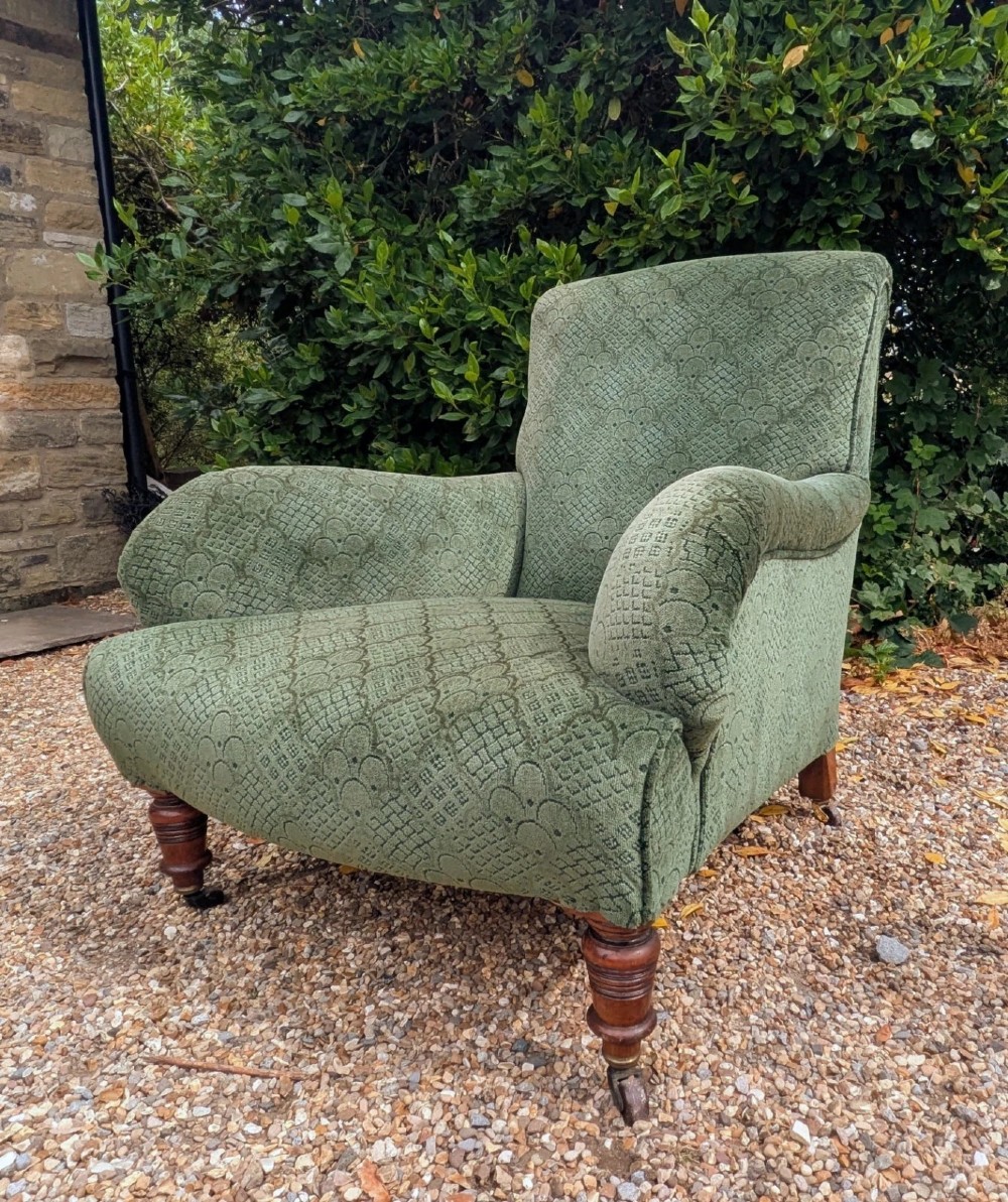 A low-slung 19th-century Howard style armchair upholstered in patterned green fabric with turned mahogany front legs and brass castors. View V