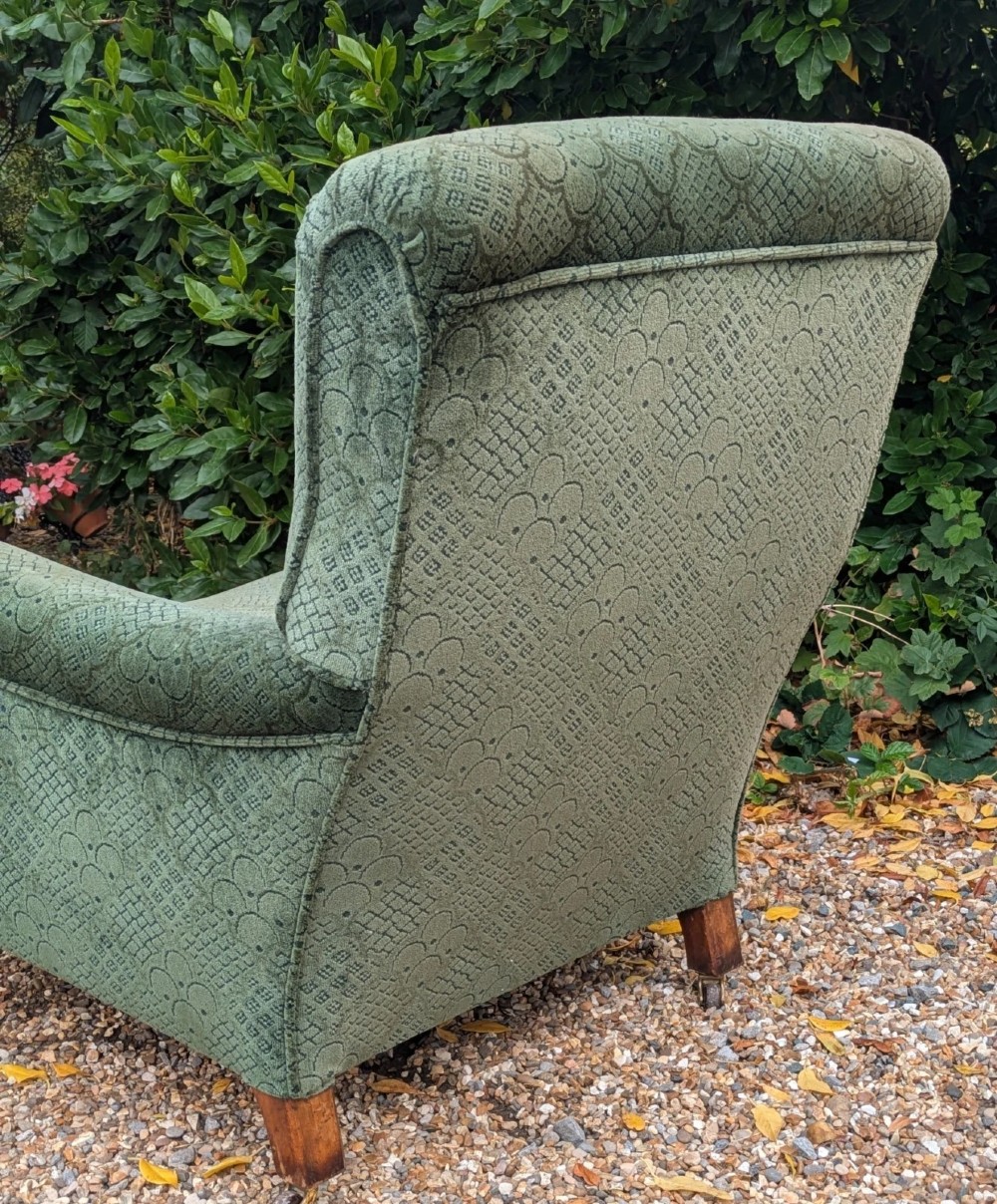 A low-slung 19th-century Howard style armchair upholstered in patterned green fabric with turned mahogany front legs and brass castors. View VI