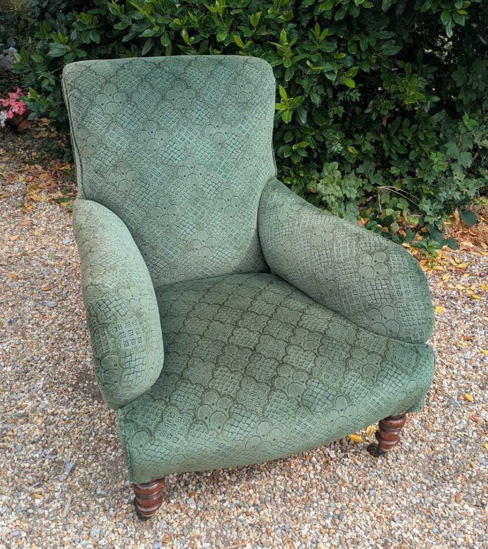 A low-slung 19th-century Howard style armchair upholstered in patterned green fabric with turned mahogany front legs and brass castors. View VII