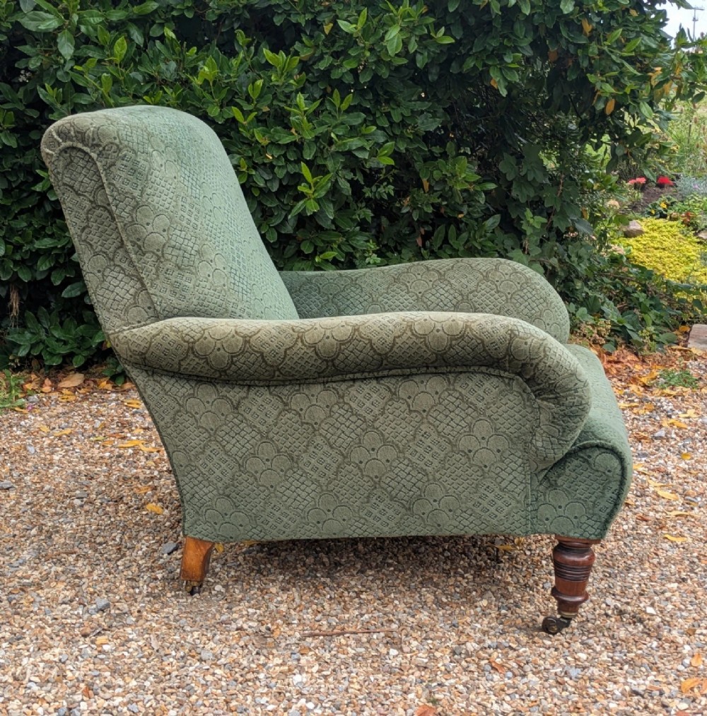 A low-slung 19th-century Howard style armchair upholstered in patterned green fabric with turned mahogany front legs and brass castors. View VIII