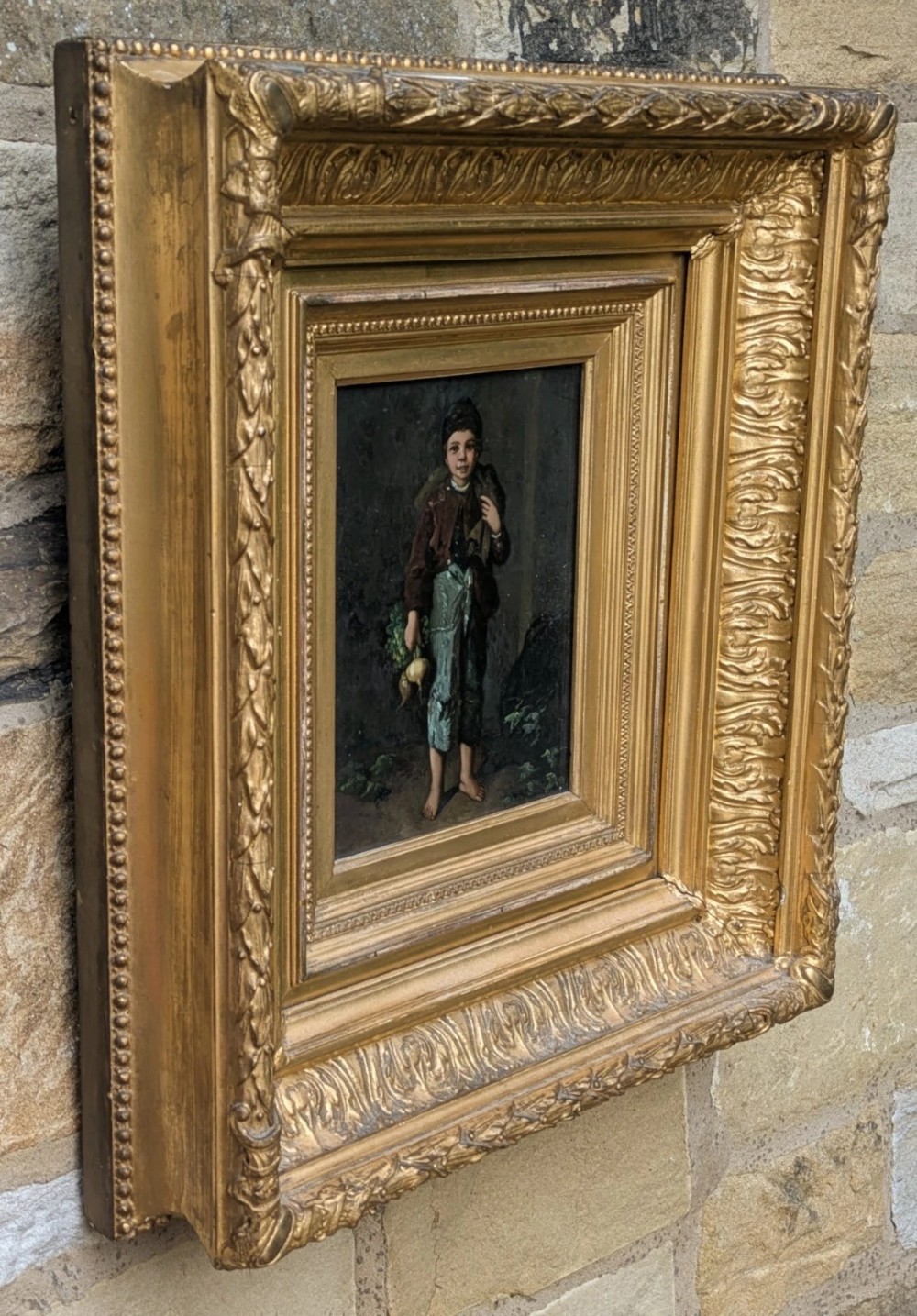 A pair of 19th-century oil paintings depicting young boys in rustic attire, mounted within deep, ornate gilded wooden frames. View V
