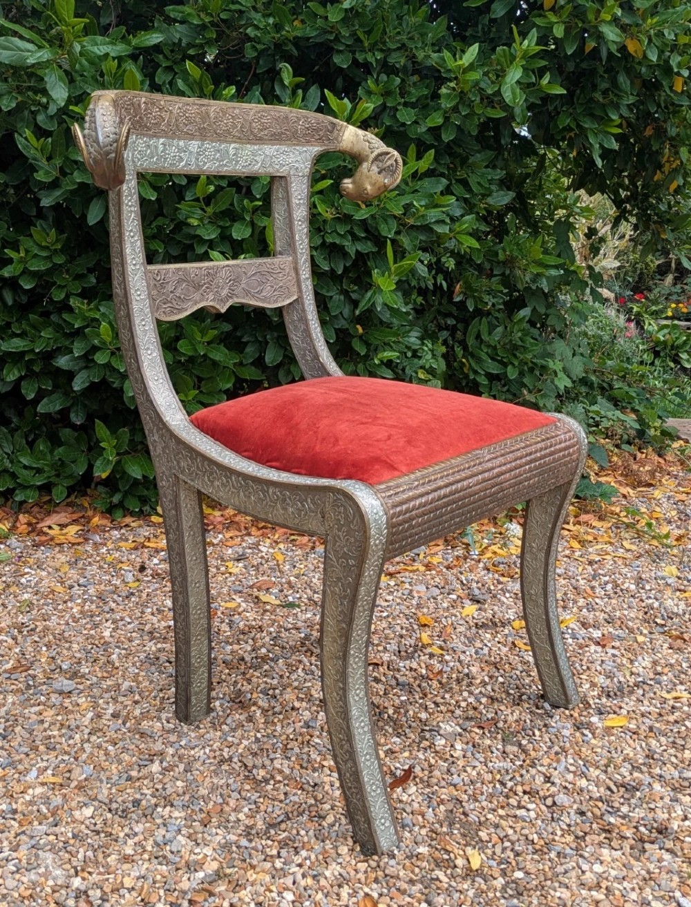 An Indian ceremonial chair wrapped in embossed silver metal with sculpted rams head terminals and a red velvet upholstered seat. View V
