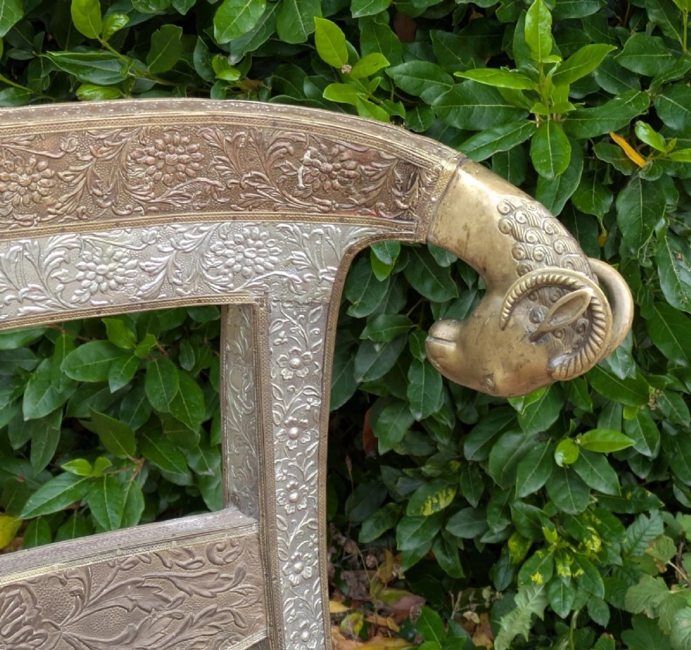 An Indian ceremonial chair wrapped in embossed silver metal with sculpted rams head terminals and a red velvet upholstered seat. View VII