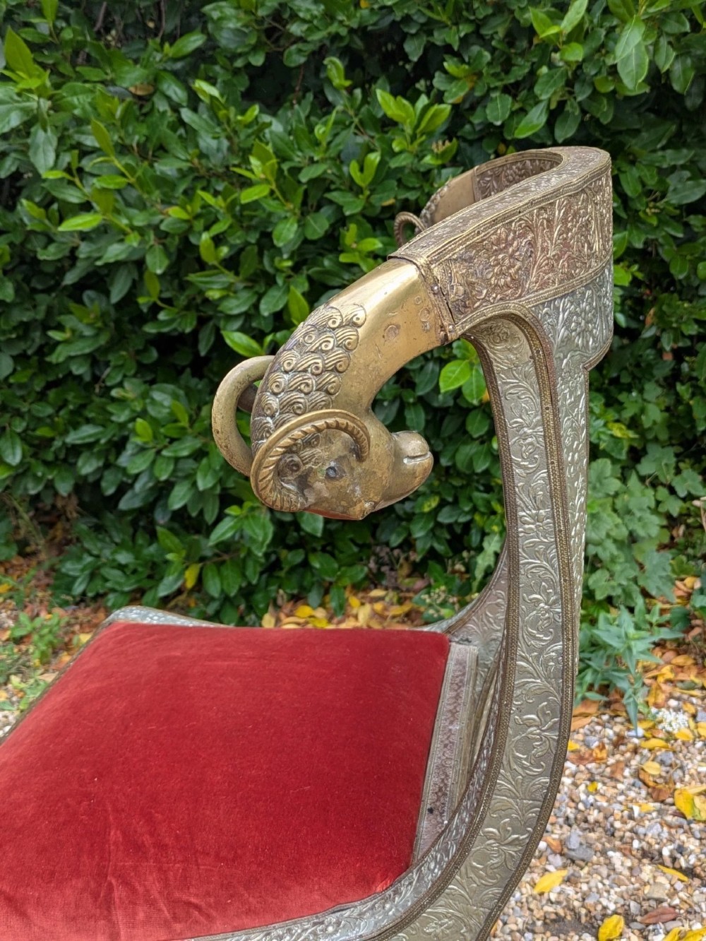 An Indian ceremonial chair wrapped in embossed silver metal with sculpted rams head terminals and a red velvet upholstered seat. View IX