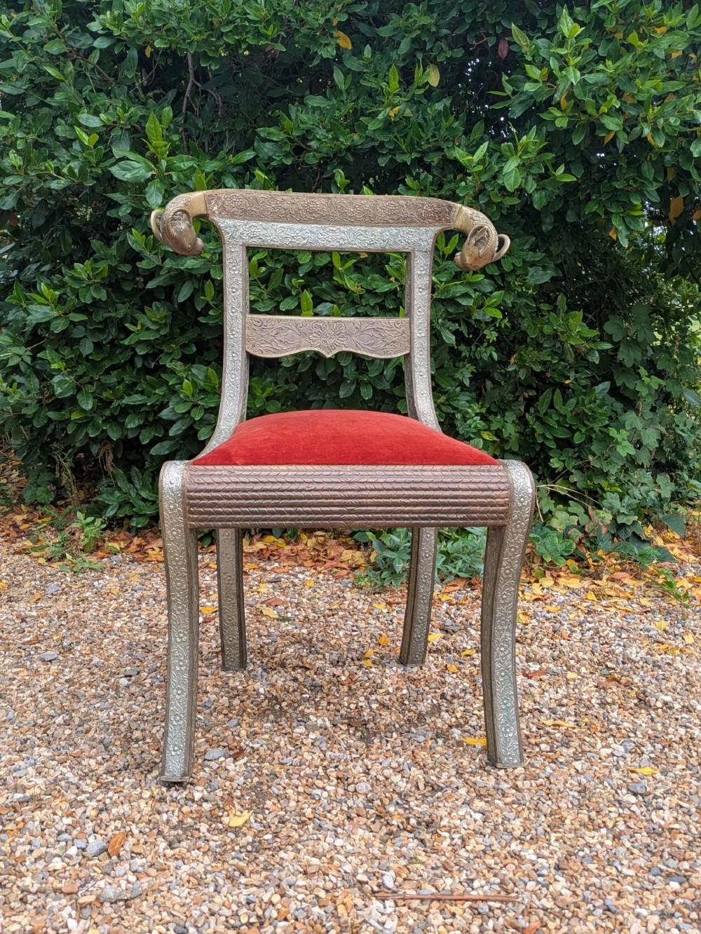An Indian ceremonial chair wrapped in embossed silver metal with sculpted rams head terminals and a red velvet upholstered seat. View X