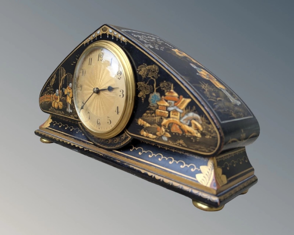A black lacquered arched mantel clock featuring hand-painted gold Chinoiserie figures and landscapes surrounding a central brass dial. View VI