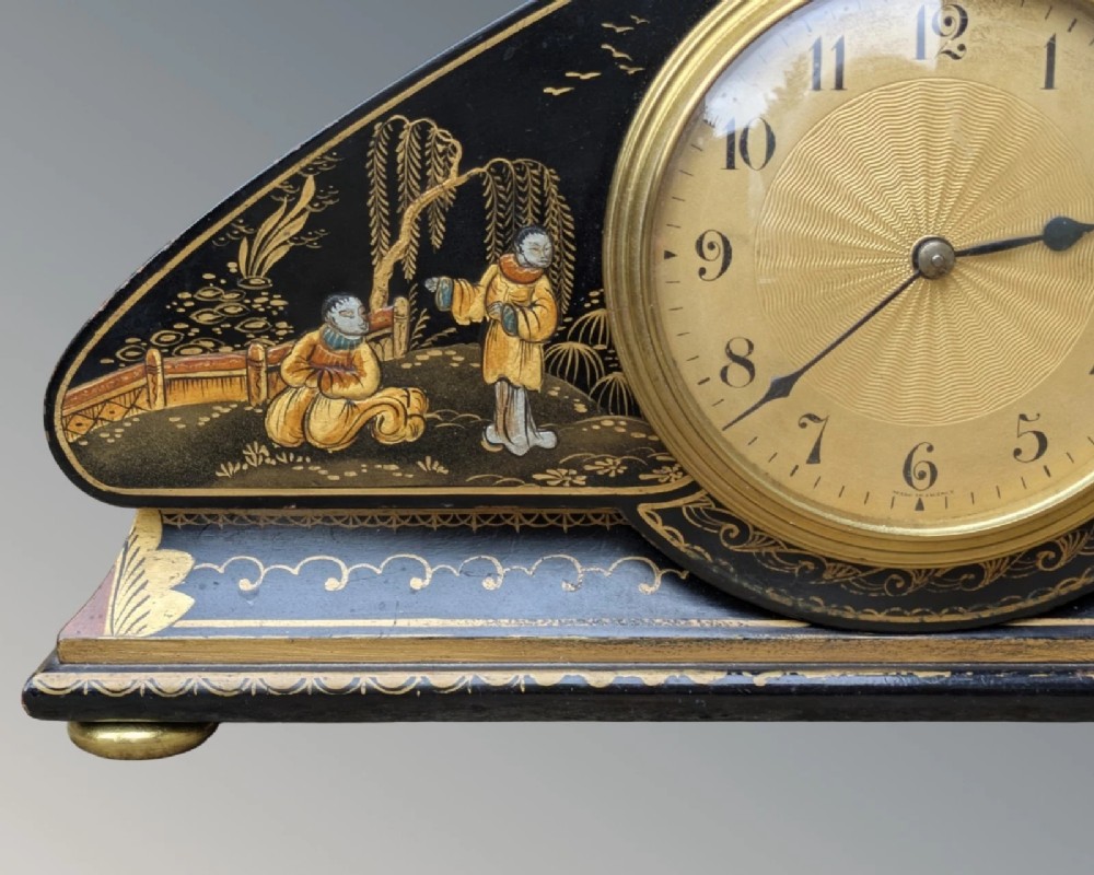 A black lacquered arched mantel clock featuring hand-painted gold Chinoiserie figures and landscapes surrounding a central brass dial. View IX