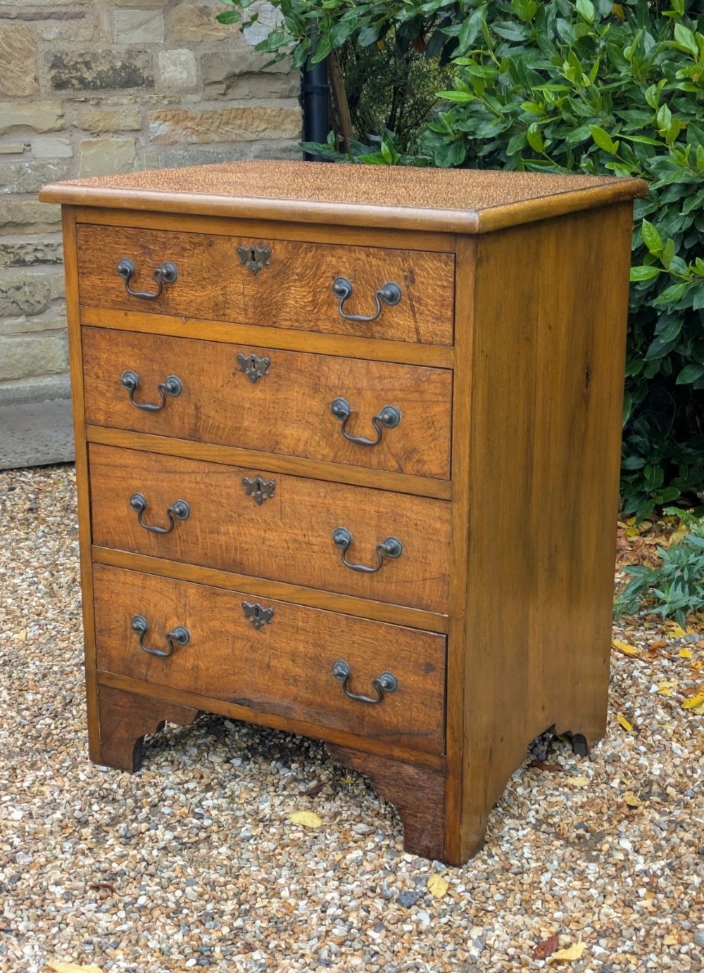 A compact oak bachelors chest of drawers featuring four graduated drawers with metal drop handles and keyhole escutcheons on a shaped bracket base. View II