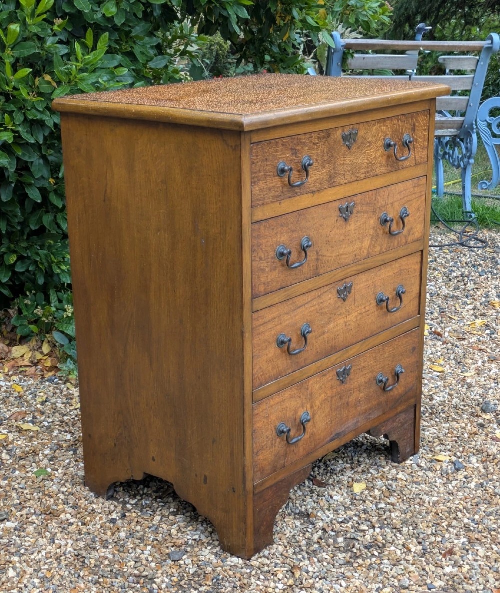 A compact oak bachelors chest of drawers featuring four graduated drawers with metal drop handles and keyhole escutcheons on a shaped bracket base. View V