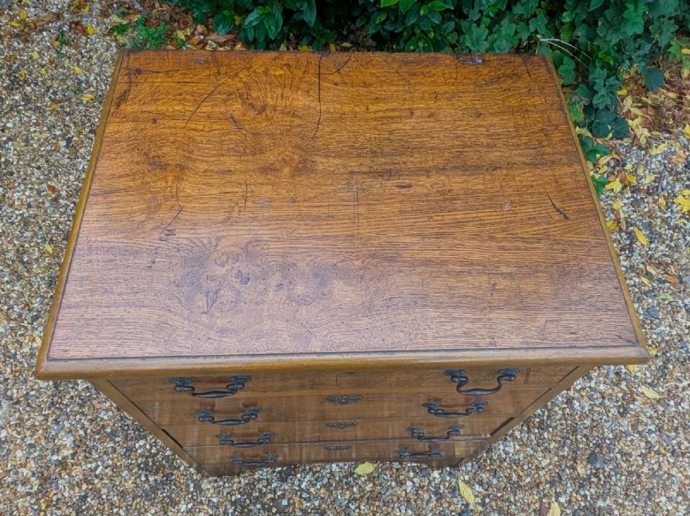 A compact oak bachelors chest of drawers featuring four graduated drawers with metal drop handles and keyhole escutcheons on a shaped bracket base. View VI
