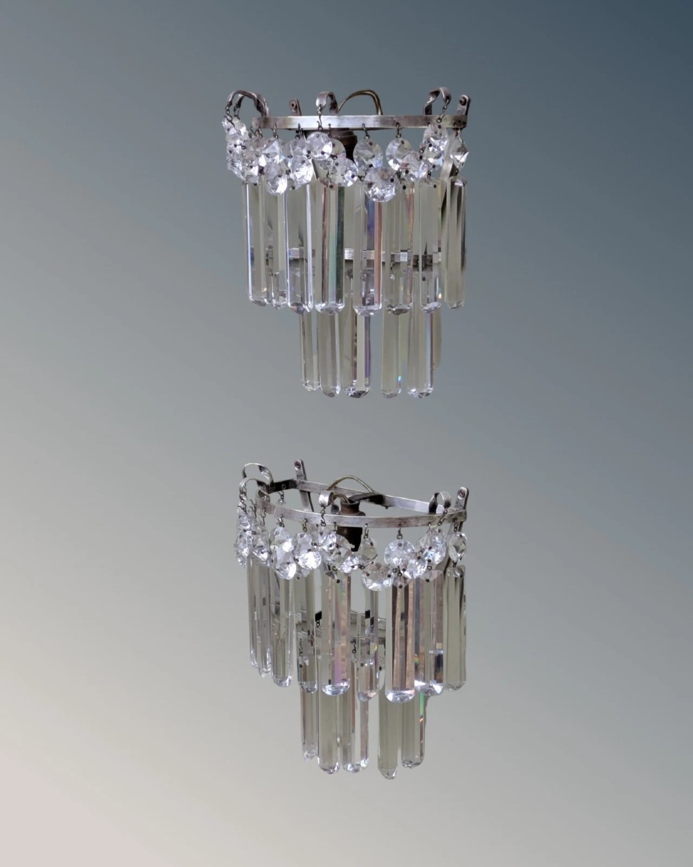 A pair of semi-circular wall lights featuring cascading tiers of clear cut crystal rectangular prisms suspended from silver-toned metal frames. View VI