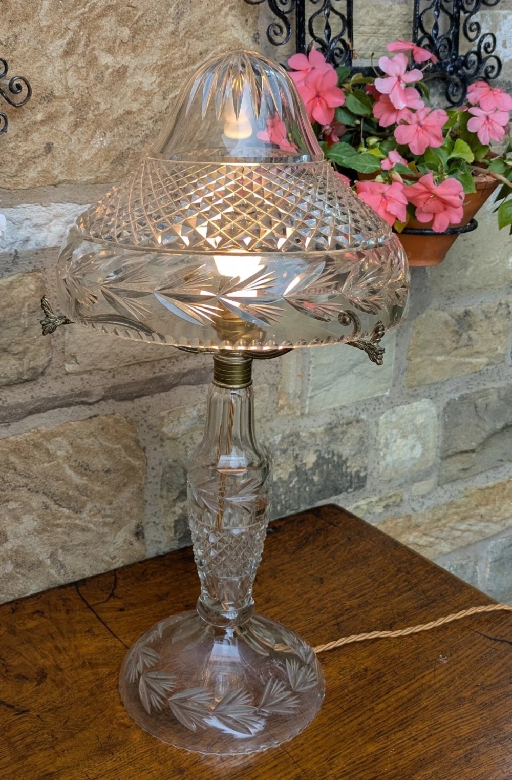 An antique cut crystal table lamp featuring a diamond-cut dome shade, a faceted baluster stem, and brass fittings.