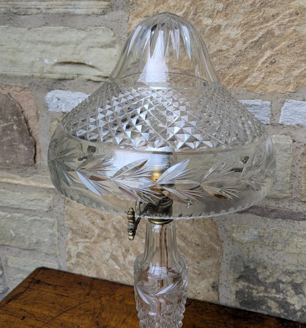 An antique cut crystal table lamp featuring a diamond-cut dome shade, a faceted baluster stem, and brass fittings. View V