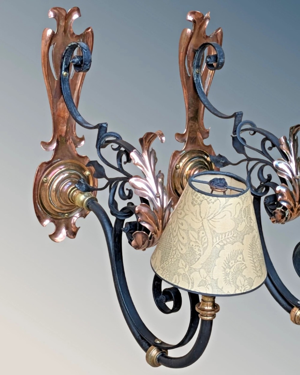 A pair of antique Arts and Crafts wall lights featuring shaped copper backplates, hand-forged black wrought iron scrollwork arms, copper leaf accents, and patterned fabric tapered shades. View II