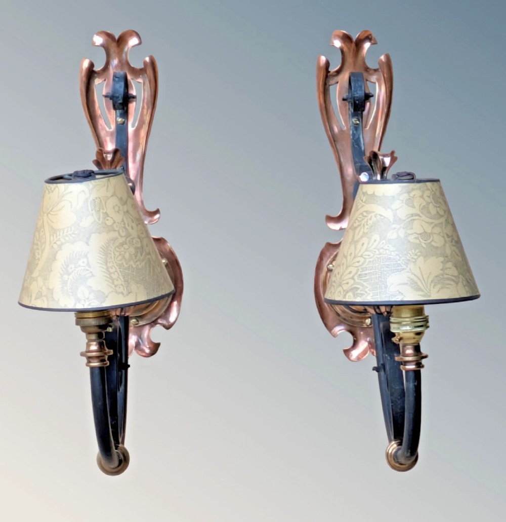A pair of antique Arts and Crafts wall lights featuring shaped copper backplates, hand-forged black wrought iron scrollwork arms, copper leaf accents, and patterned fabric tapered shades. View V