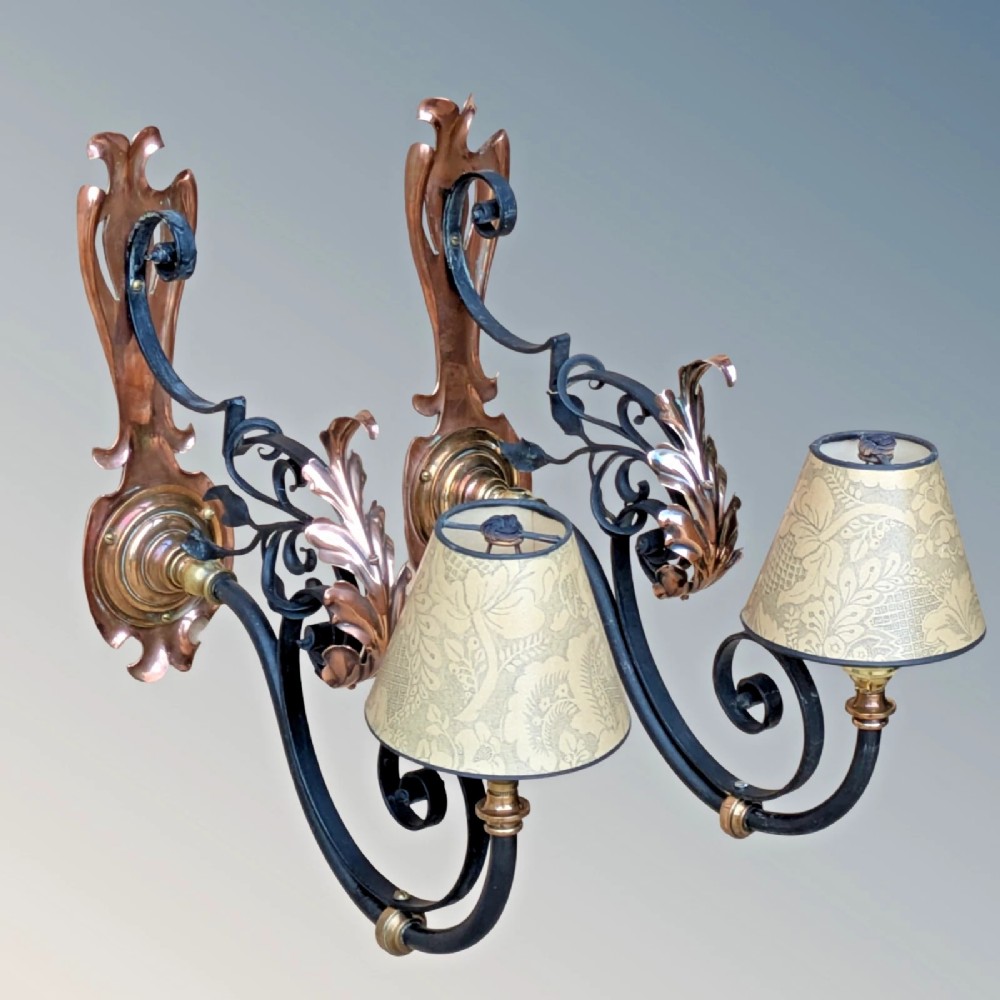 A pair of antique Arts and Crafts wall lights featuring shaped copper backplates, hand-forged black wrought iron scrollwork arms, copper leaf accents, and patterned fabric tapered shades. View VI