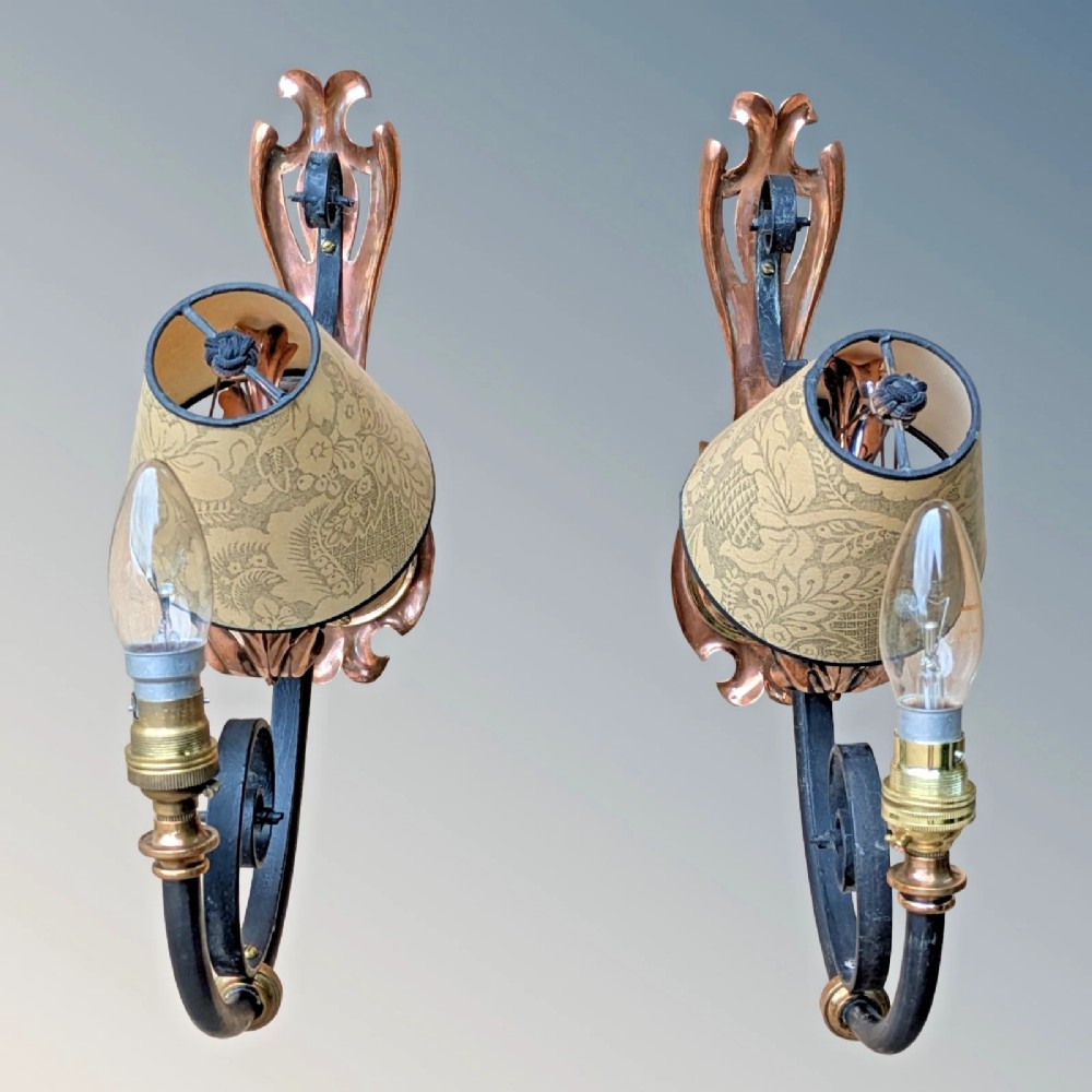 A pair of antique Arts and Crafts wall lights featuring shaped copper backplates, hand-forged black wrought iron scrollwork arms, copper leaf accents, and patterned fabric tapered shades. View VII