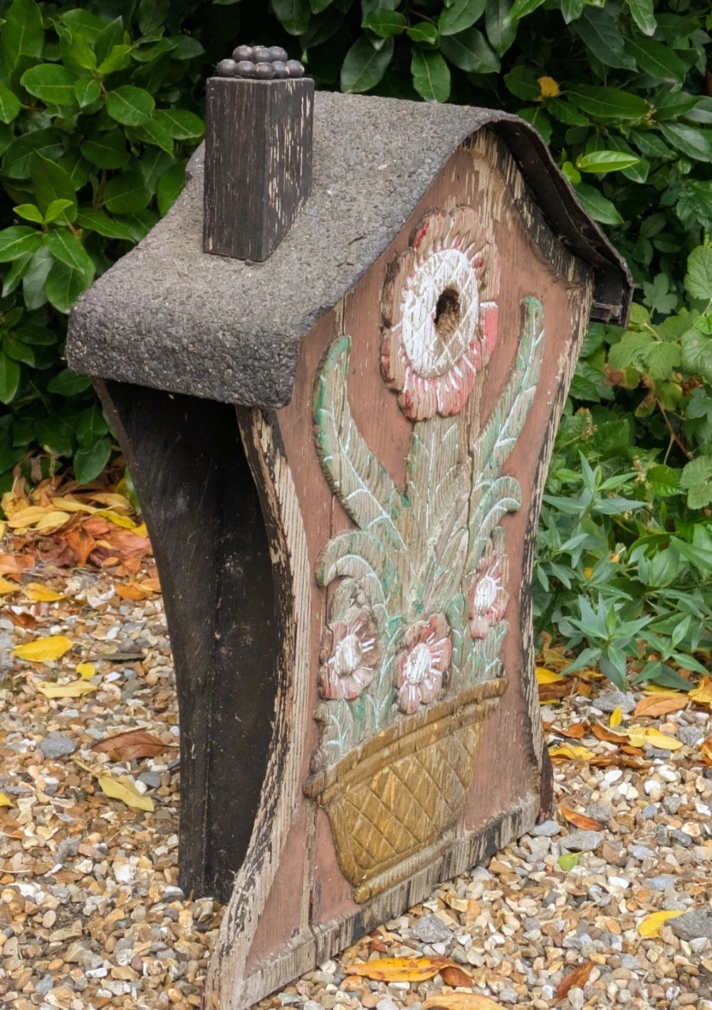 A carved and painted wooden Swedish birdhouse featuring a floral motif in a pot with a central entry hole and a chimney detail. View II